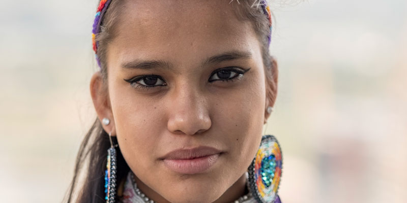 A close-up of a young woman wearing beaded earrings, necklace and headband