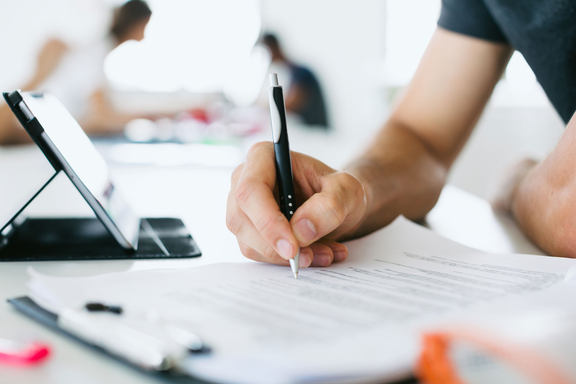 Person writing in an airy office setting with others working in the background