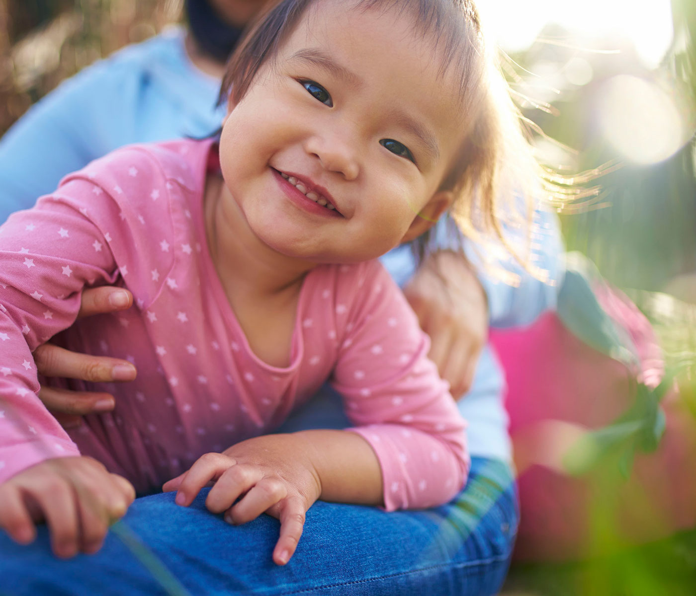 Child Smiling in Parent's Lap with Sun Shining Behind Them