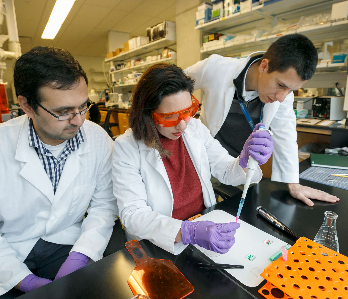 Three scientists looking at a pipette