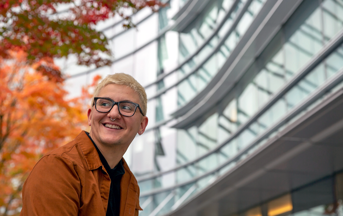 Student sitting outside with fall leaves in background