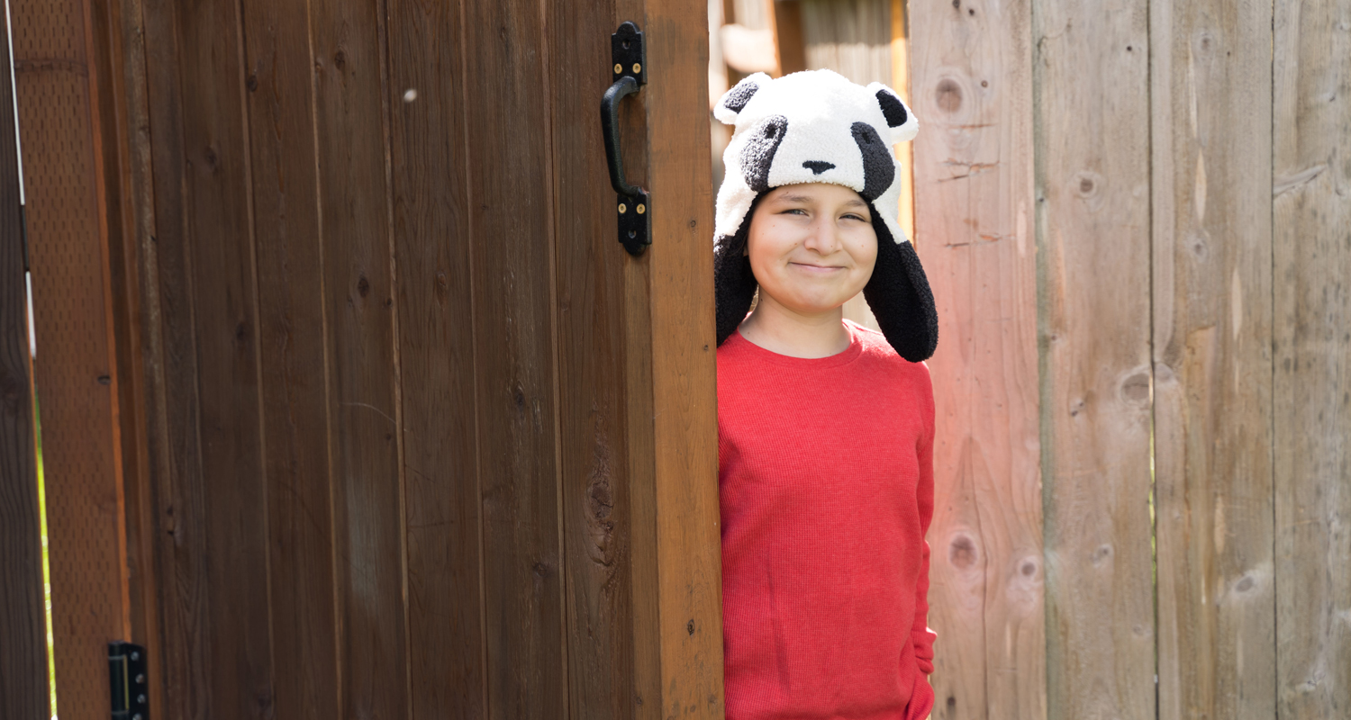boy with a silly panda hat stands inside a wooden gate
