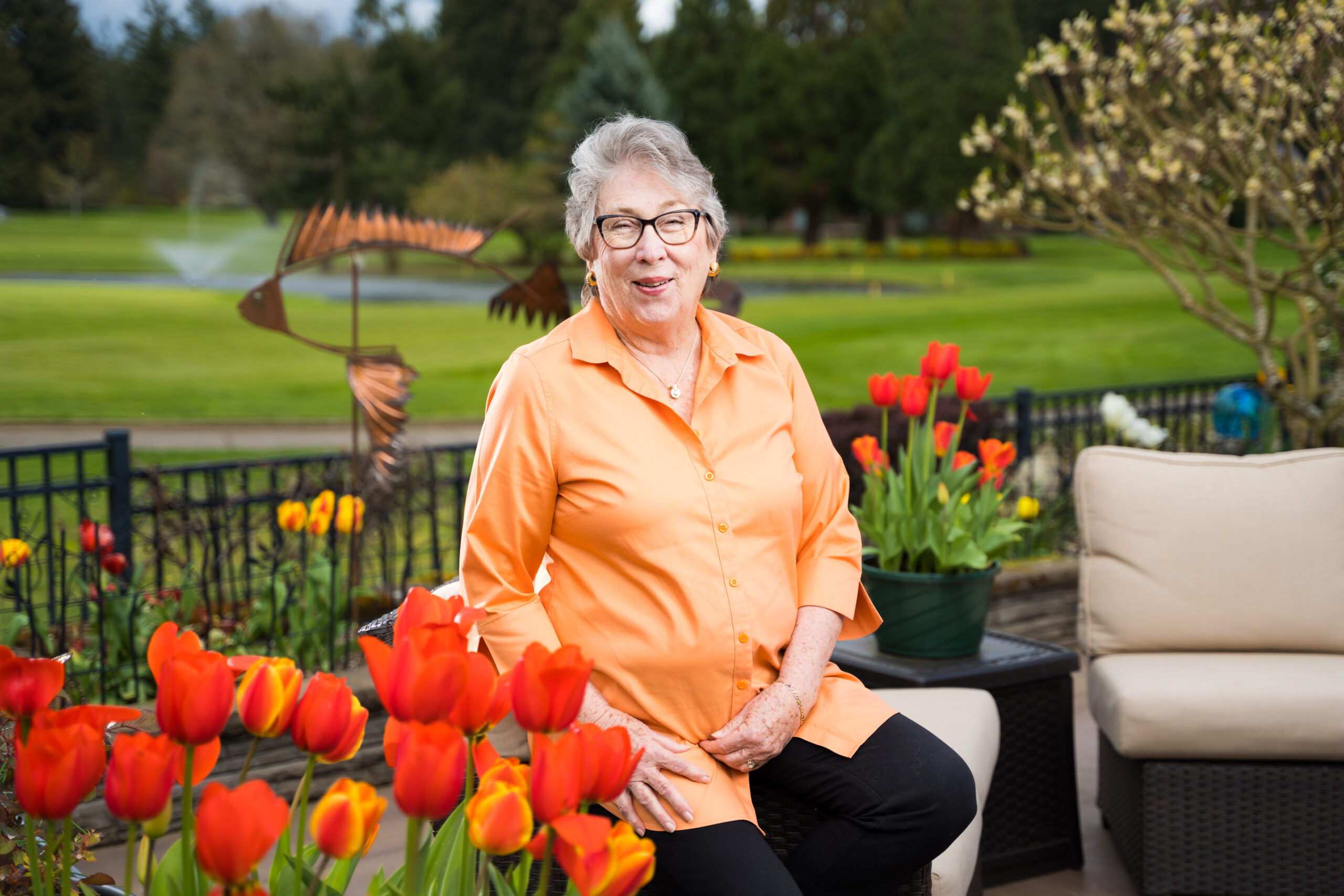 Older woman sits in her garden surrounded by red tulips
