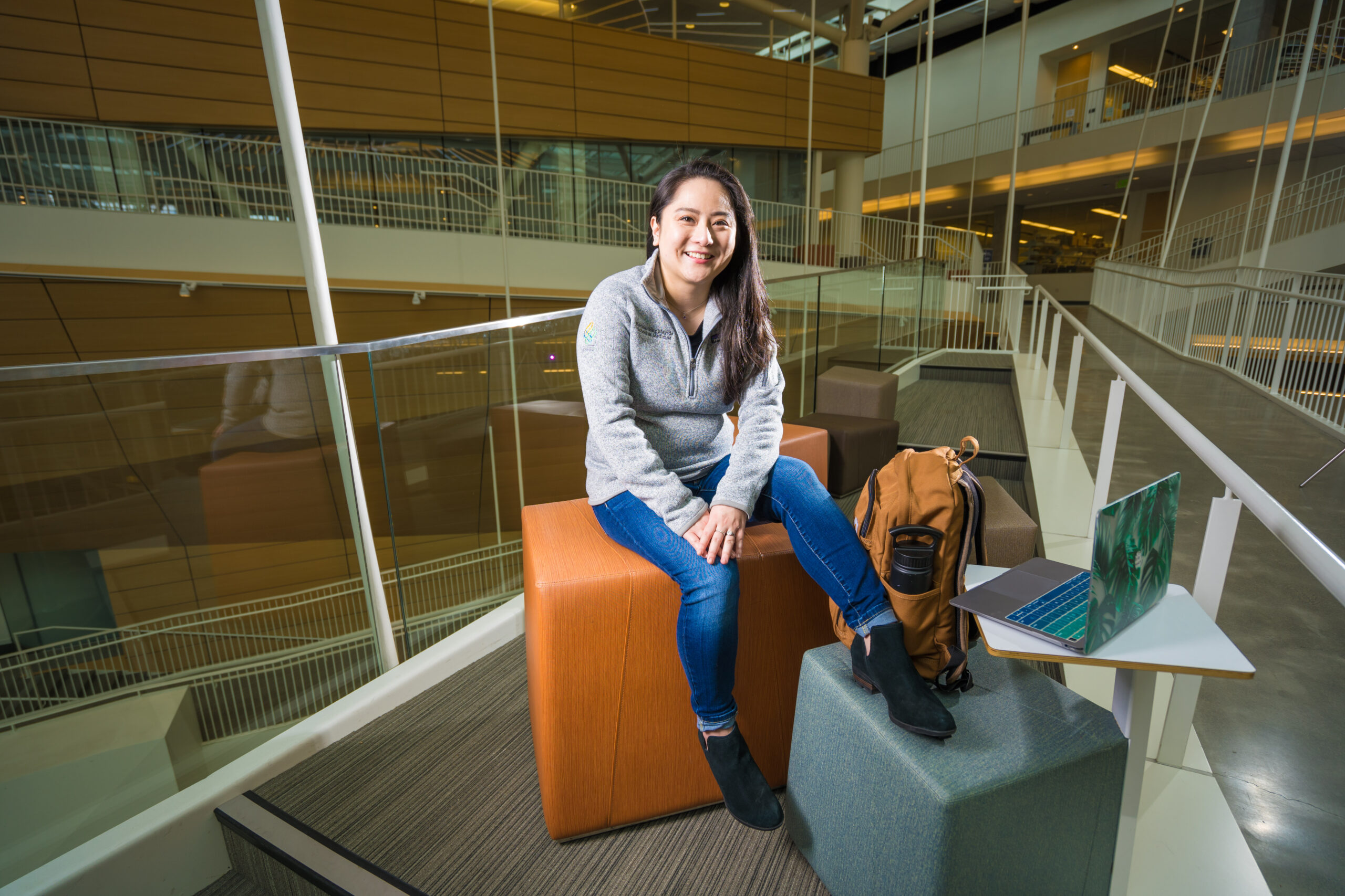 Smiling young woman sits in the Robertson Life Sciences Building with her foot propped up
