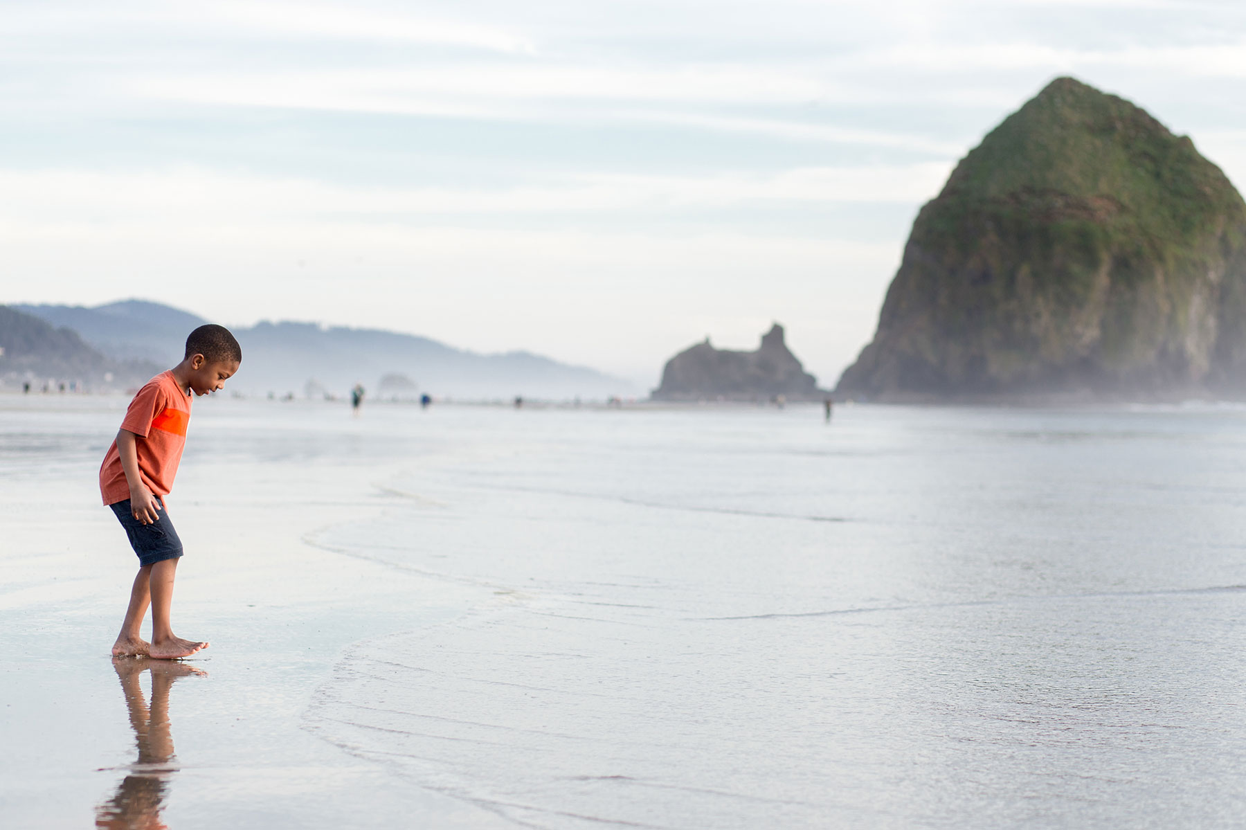 A Black child plays in the ocean with Haystack Rock in the background