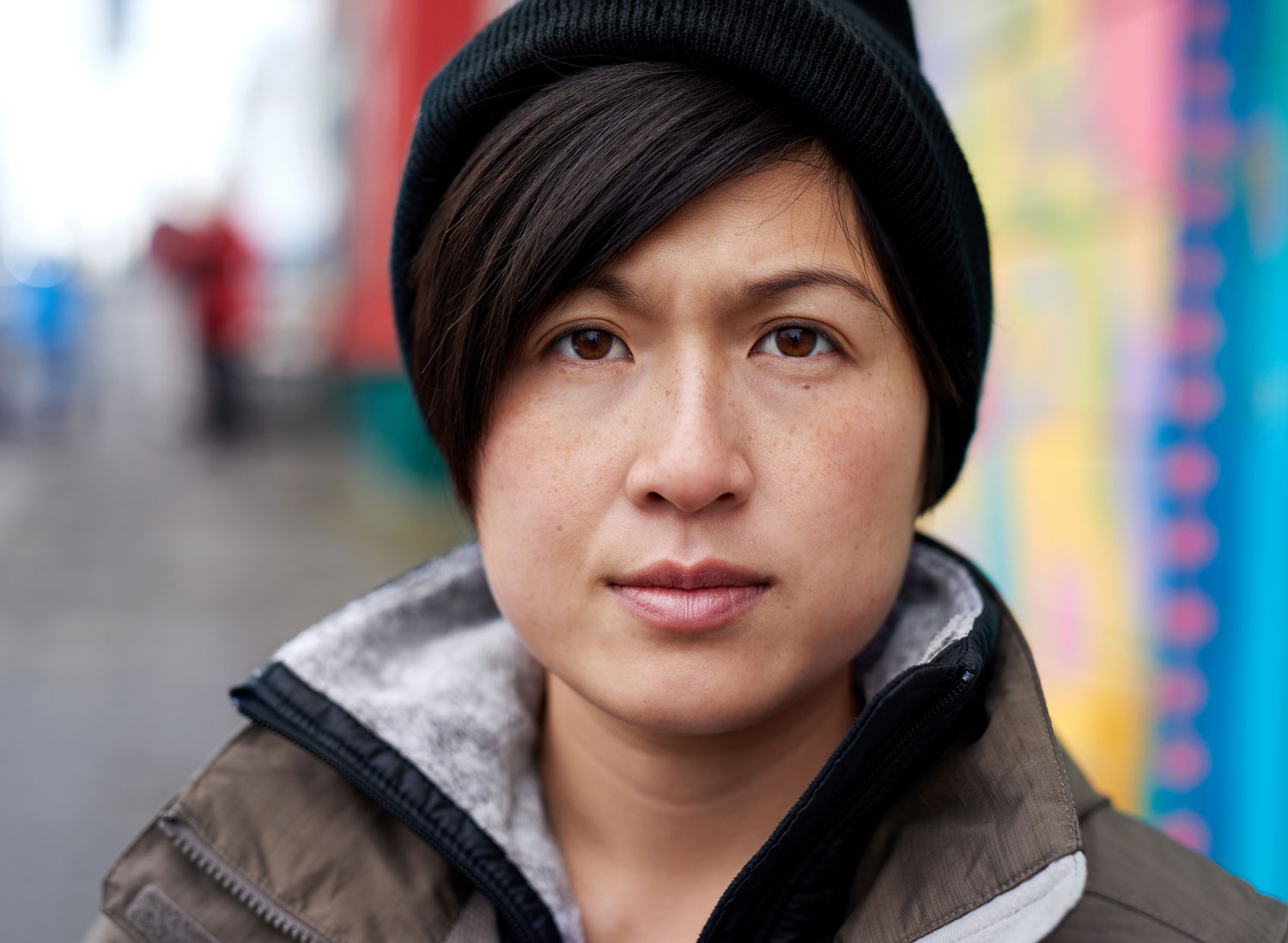 Asian woman with stocking cap looks directly at camera with defiant expression