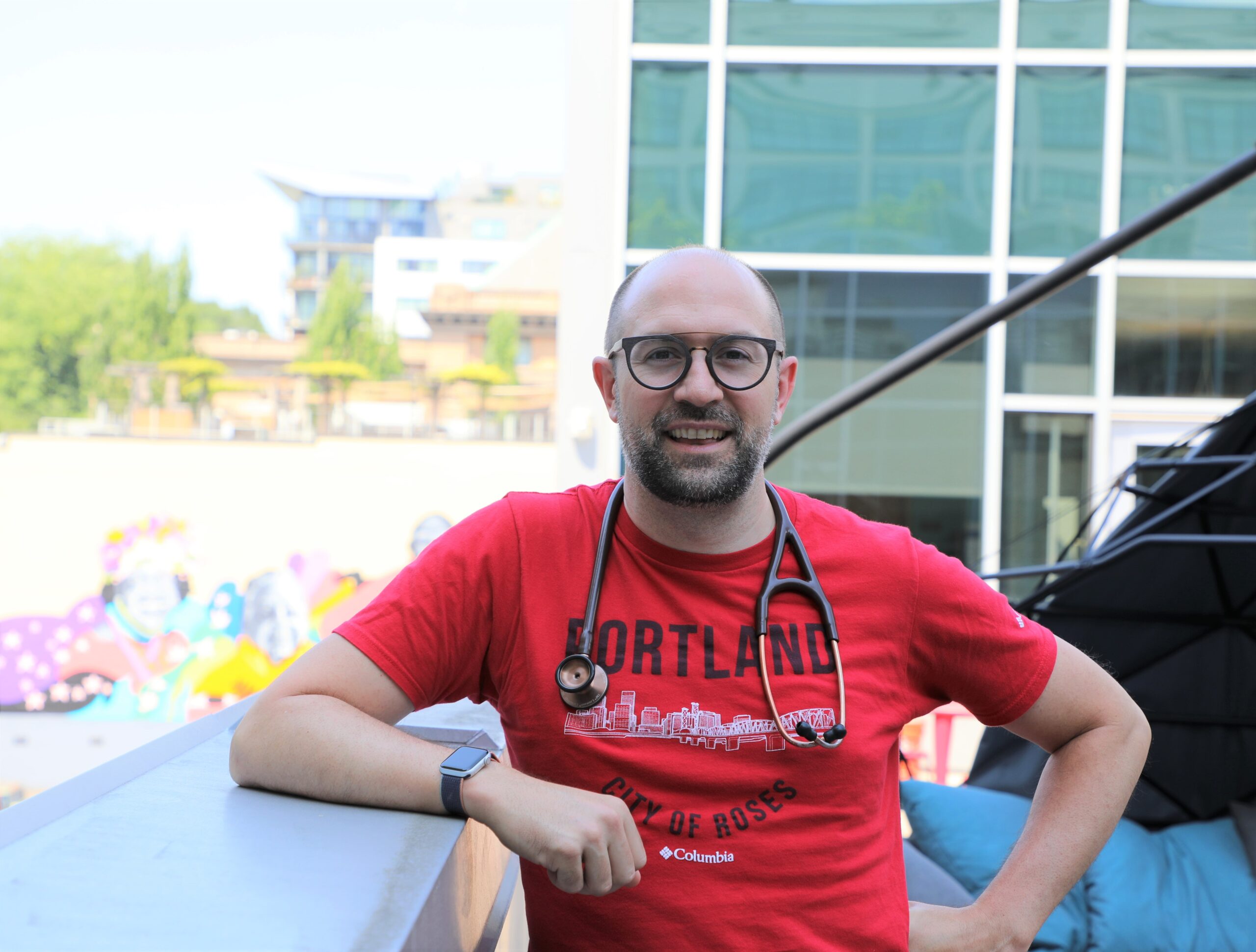 Alum Richard Bruno stands smiling with red shirt and stethoscope.