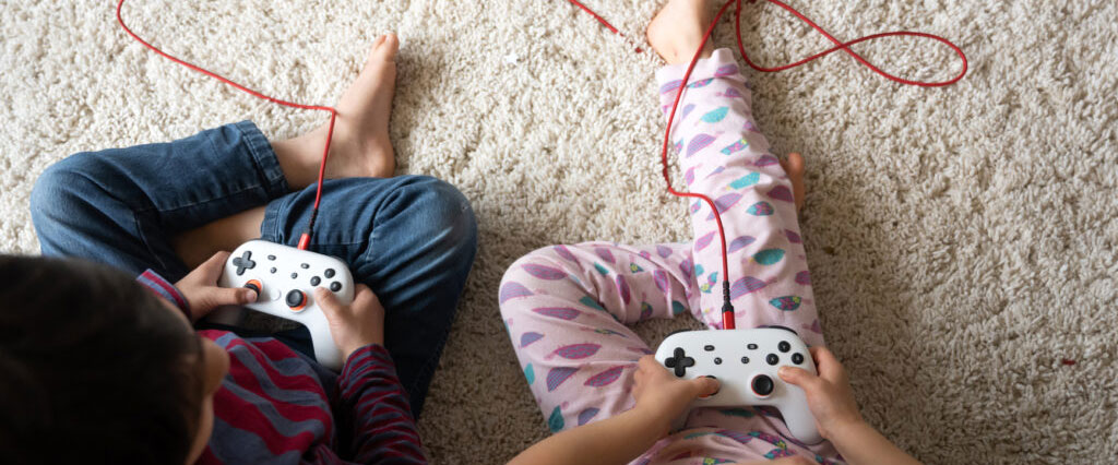 Two young children sit on carpet with video game consoles.