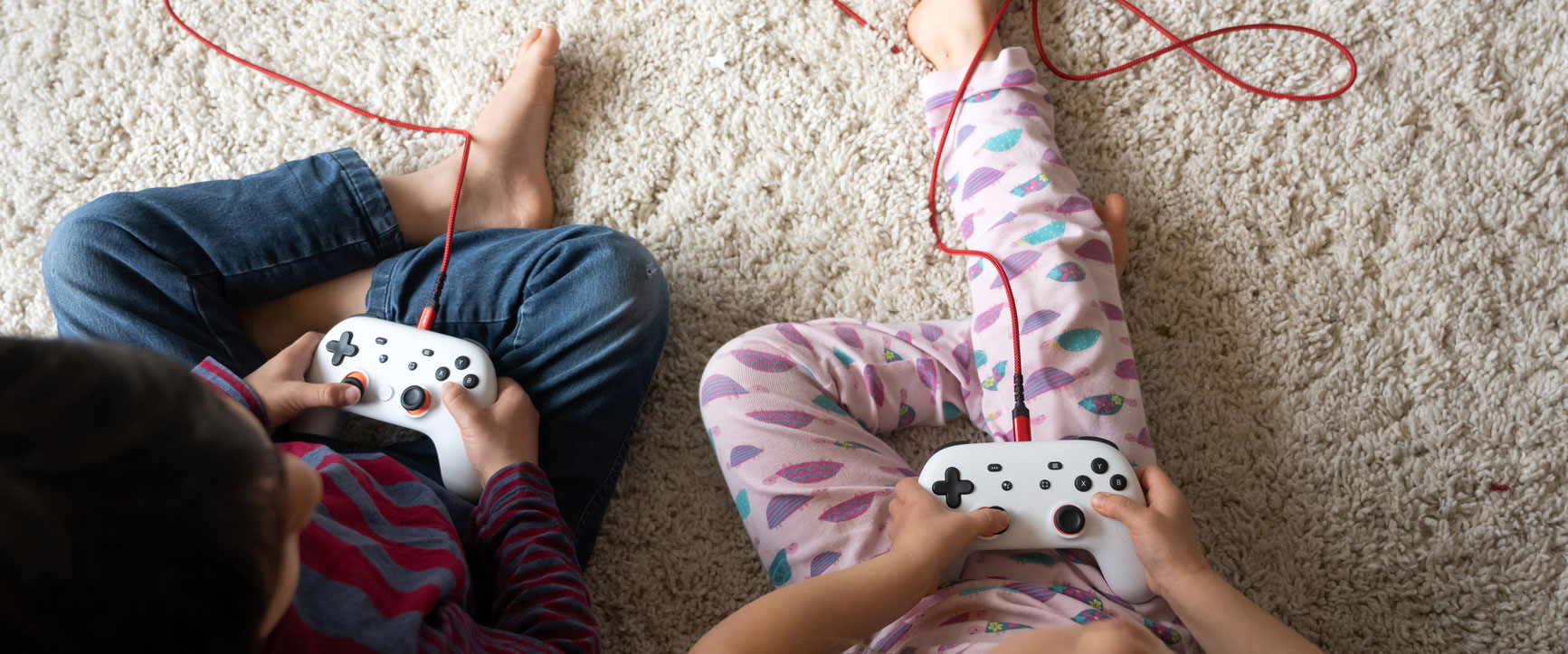 Two young children sit on carpet with video game consoles.