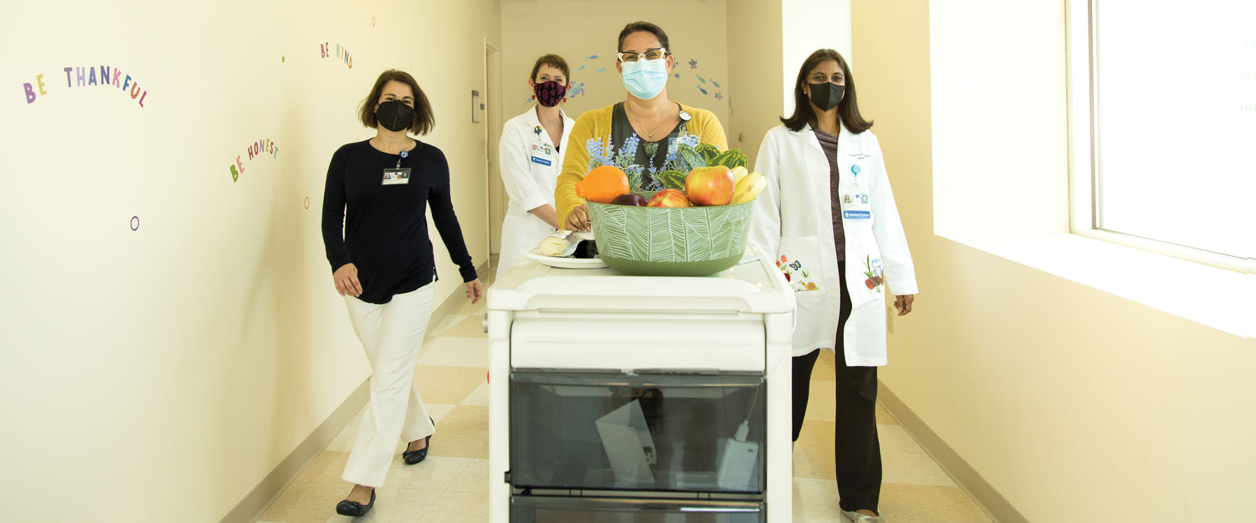 Doctors rolling down a hospital corridor with fresh fruit on a cart