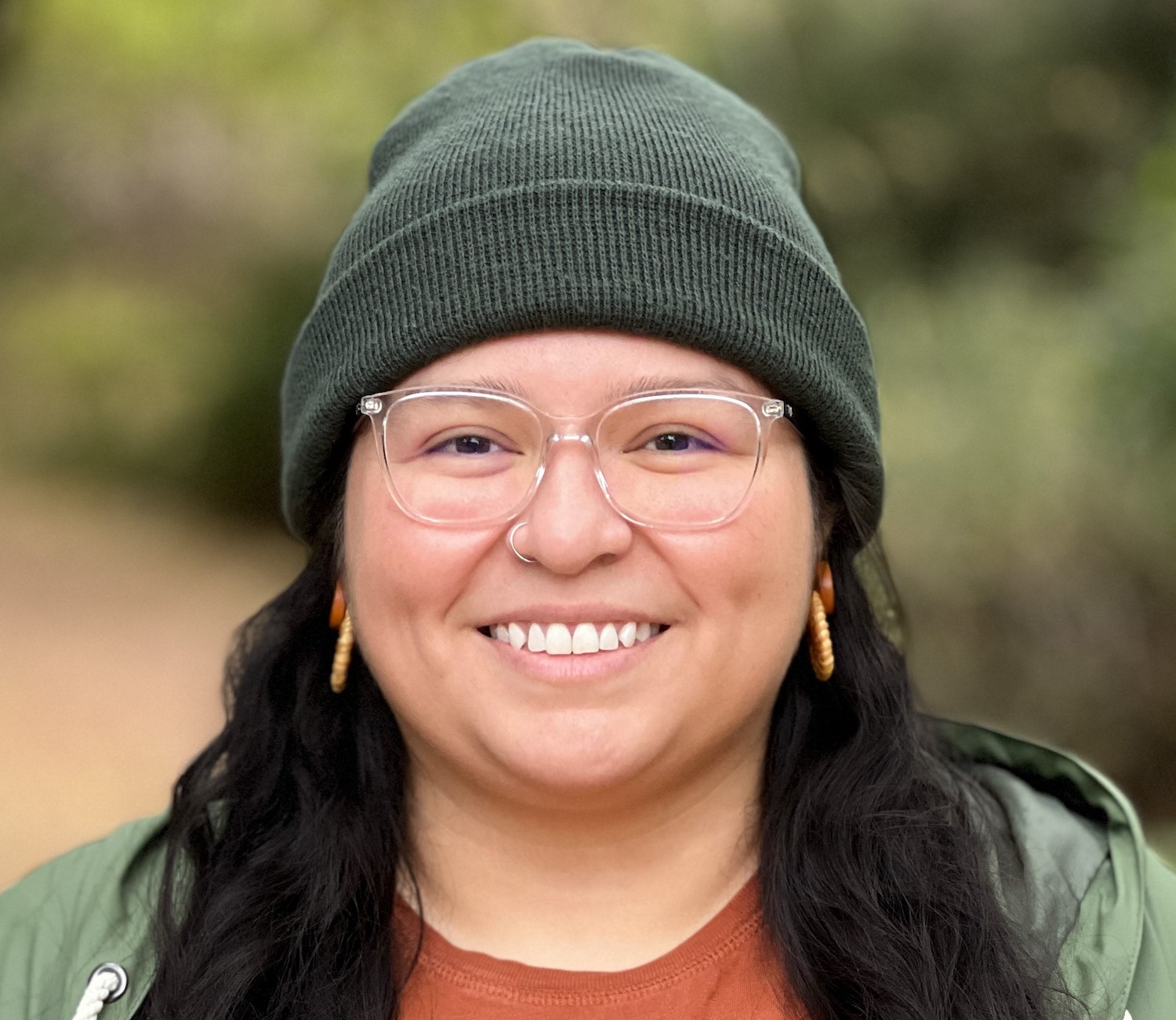 Headshot of employee, Flor Chavez, who has long dark hair, wearing glasses, green beanie, and orange crew neck shirt.