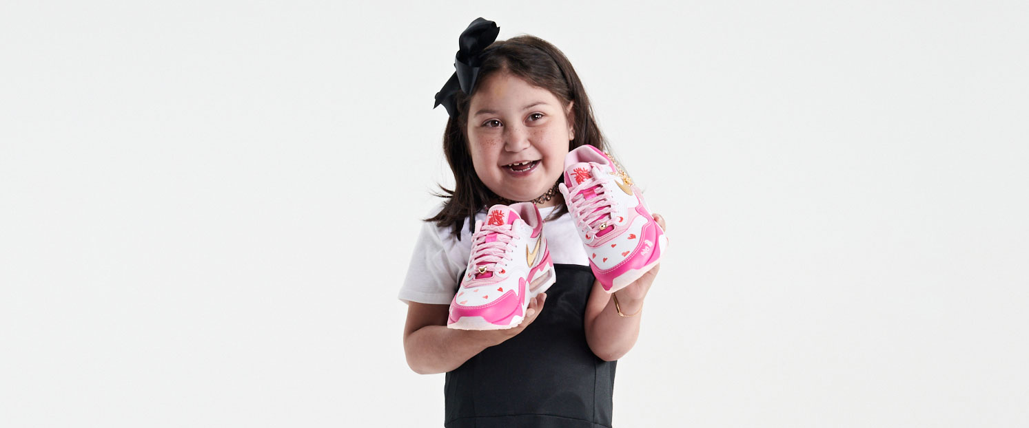 Hailey wears a black dress and holds her Doernbecher Freestyle shoes