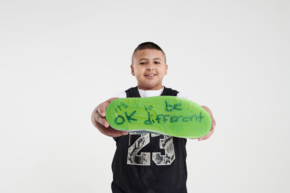 Hugo shows off the sole of his shoe, which is translucent green with the words "it's OK to be different" in his handwriting.