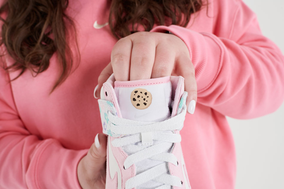 The tongue of Macey's pink and white shoe features a chocolate chip cookie above the Nike swoosh