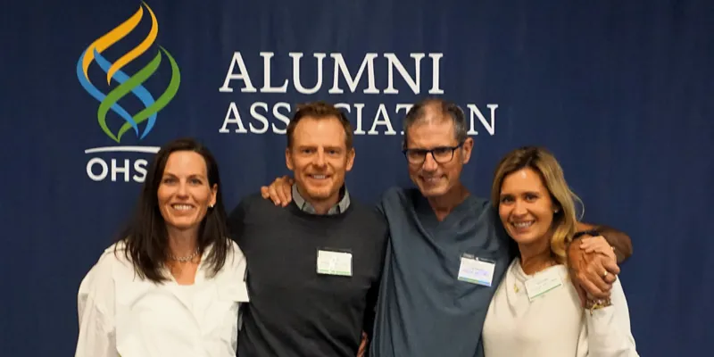 Four people smiling with arms over each others shoulders standing in front of OHSU Alumni Association banner