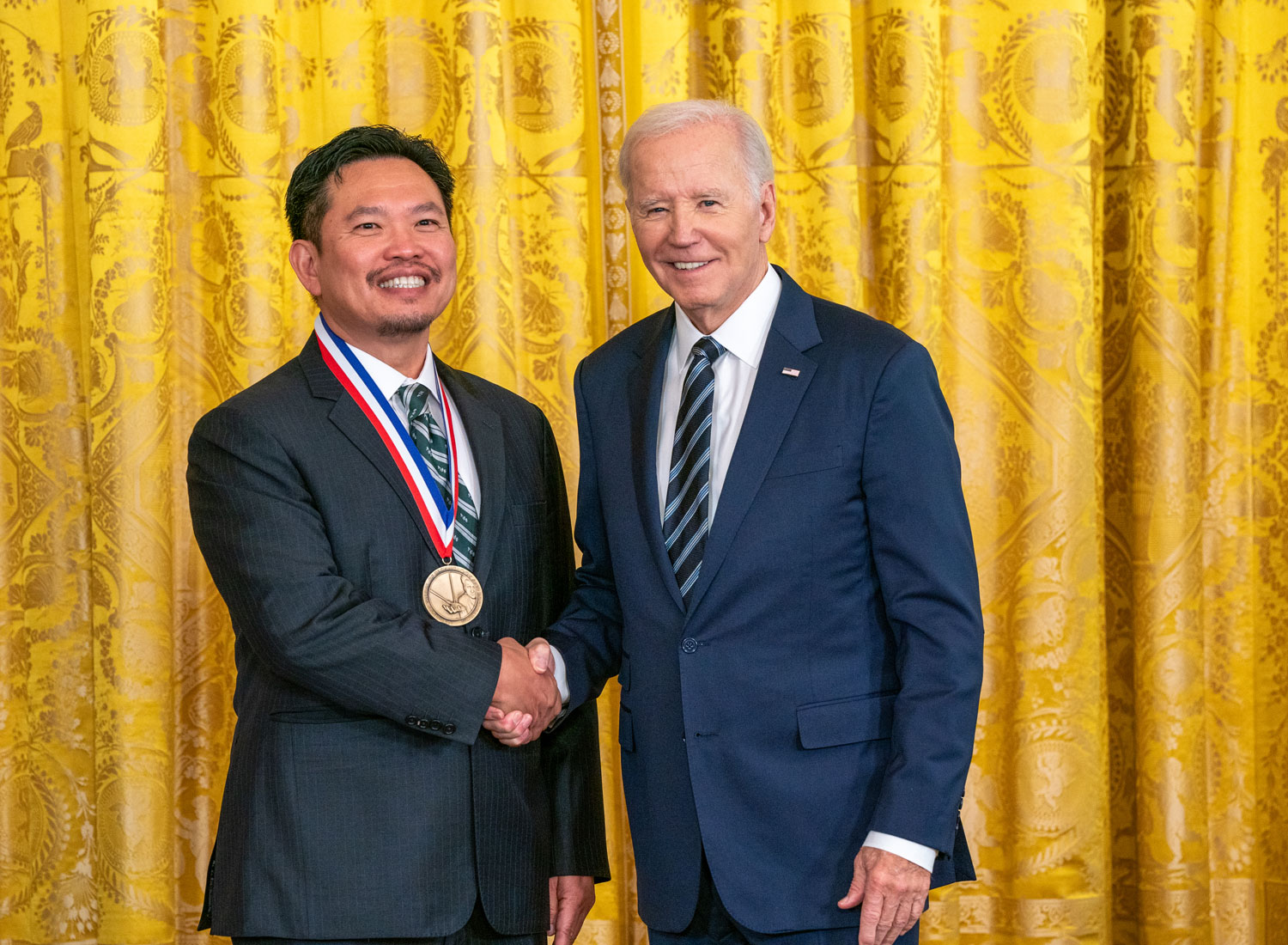 David Huang, wearing a gold medal, shakes hands with President Joe Biden.
