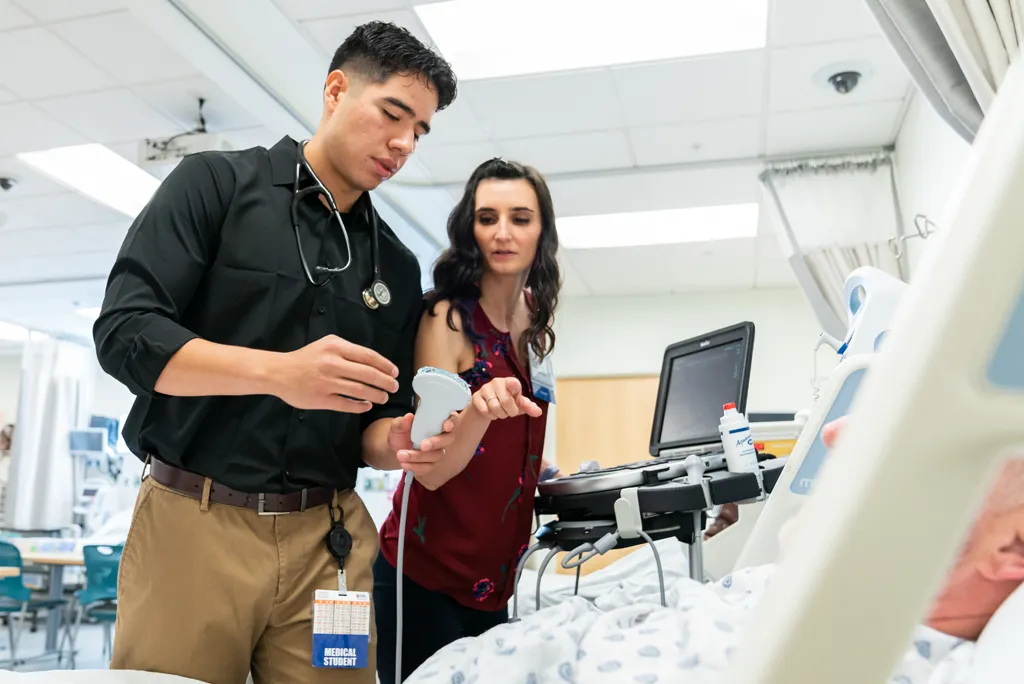 Faculty member advises school of medicine student about using an ultrasound scanner on a patient