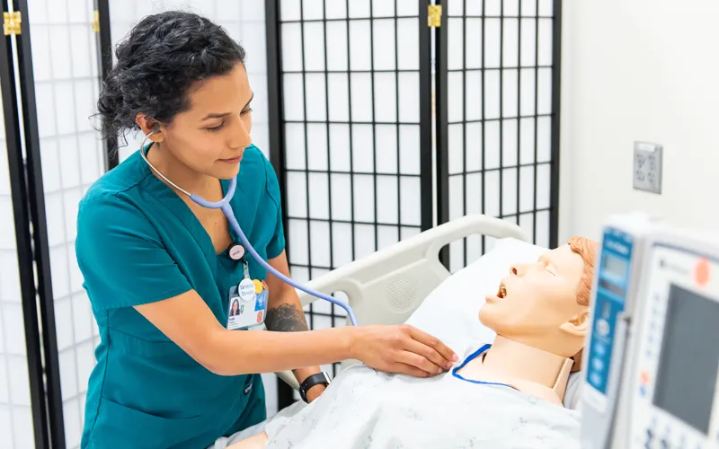 Female nursing student listens with stethoscope to manikin heartbeat.