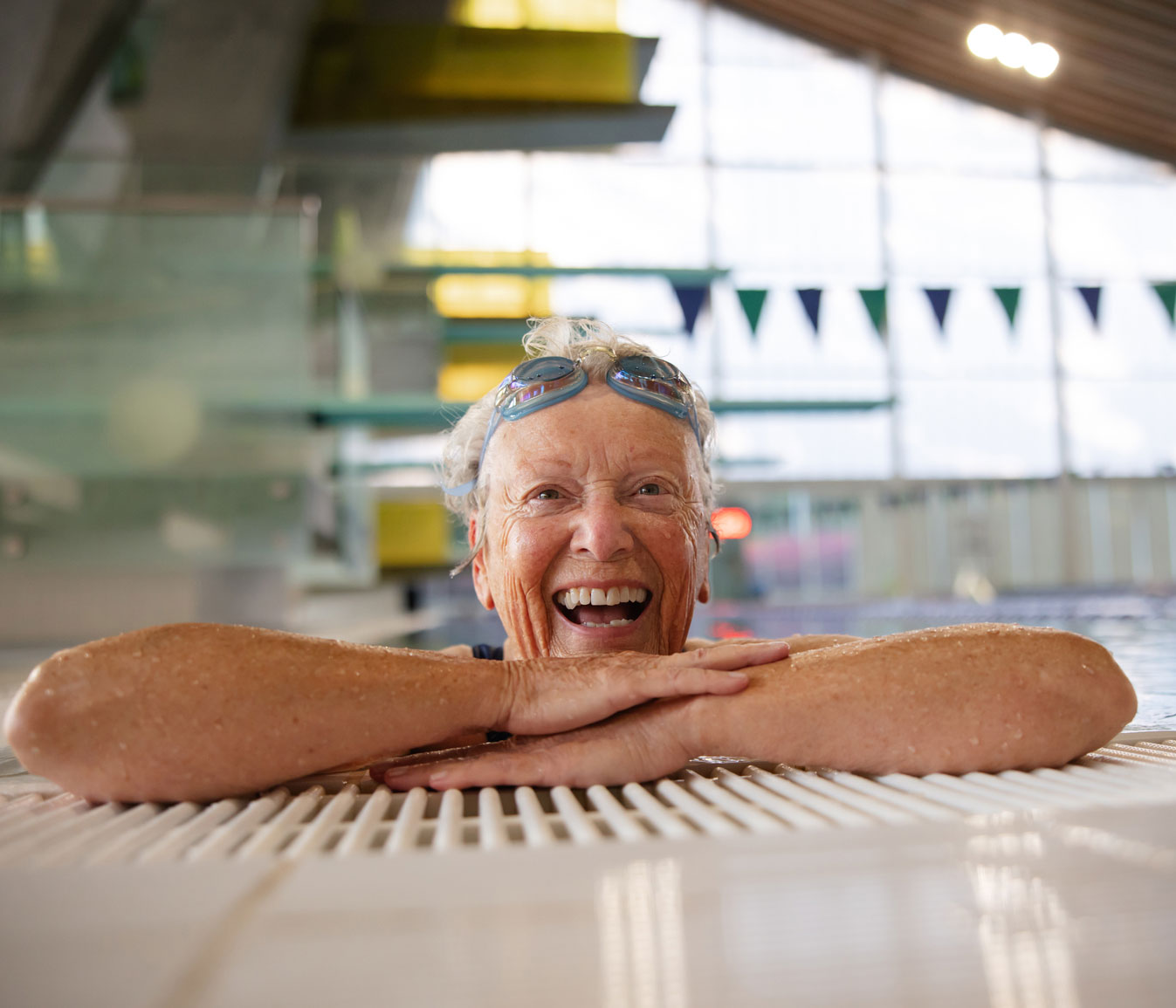 senior woman with big smile hangs off side of the swimming pool