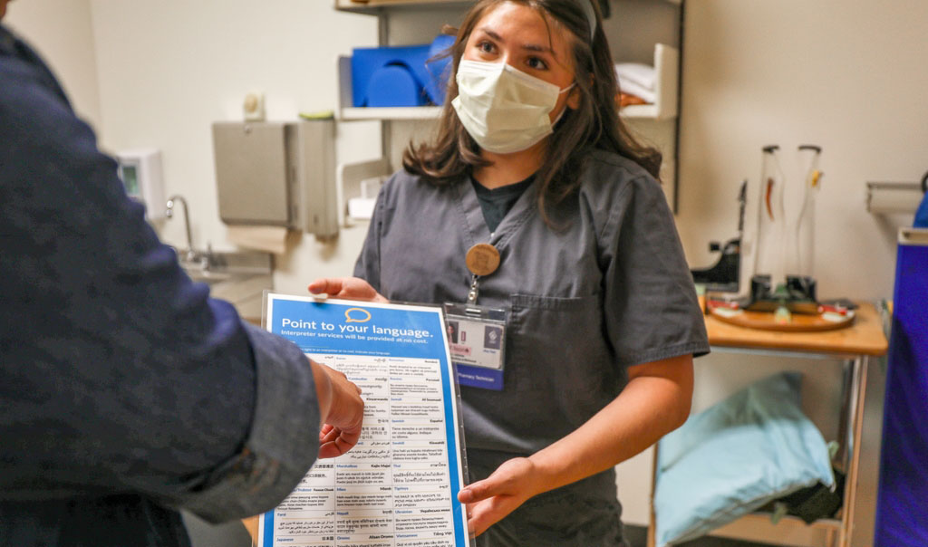 A health provider helps a patient point at which language they use on a poster.