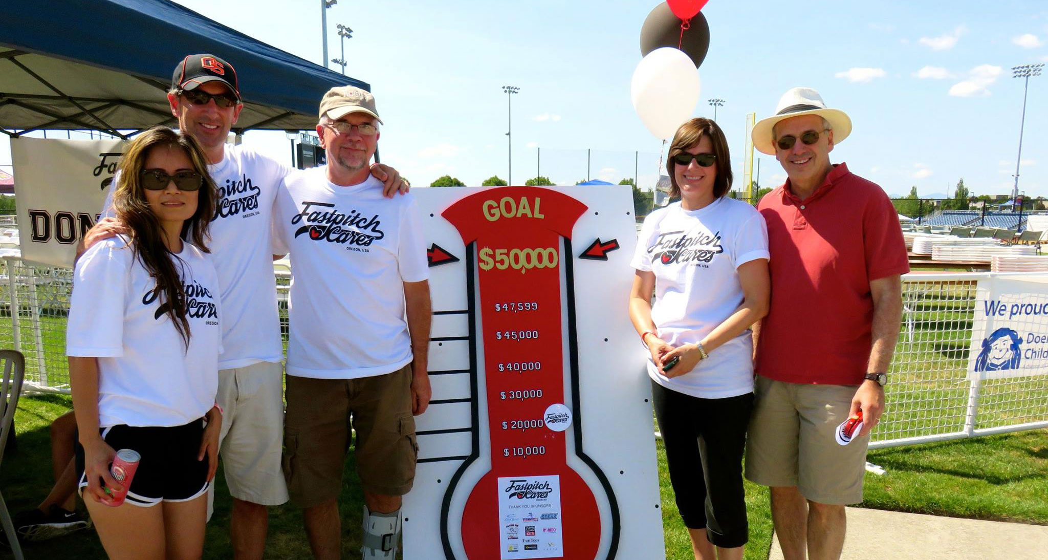 Fastpitch Cares team next to a fundraising goal sign