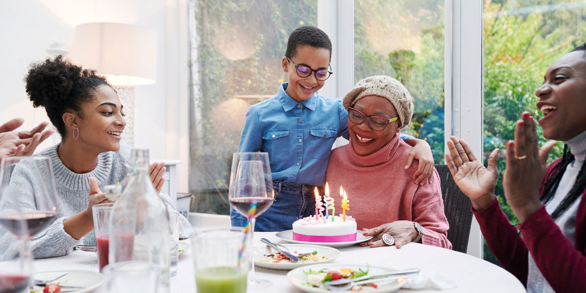 A family gathers at the table while a grandmother prepares to blow out birthday candles