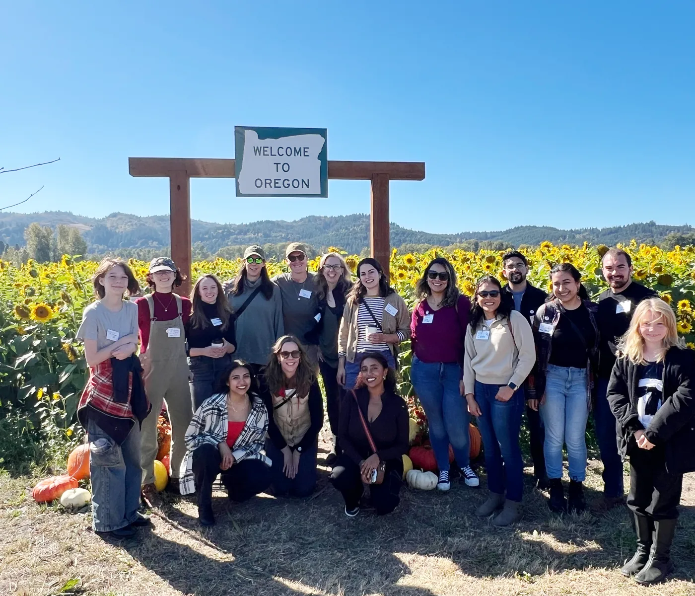 Group of PA alumni and and their families, smiling, standing outside on a sunny day in front of a sunflower field.