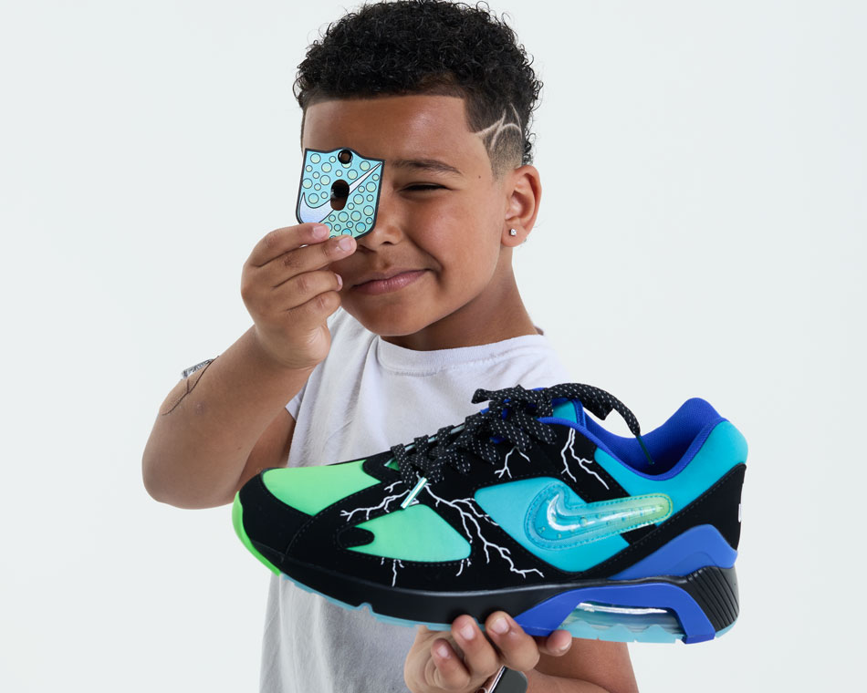 Ja'Kai Taylor holds the Nike Air 180 shoe he designed for Doernbecher Freestyle 20. The shoe is a gradient of turquoise, blues and greens with black trim and white lightning bolts. 