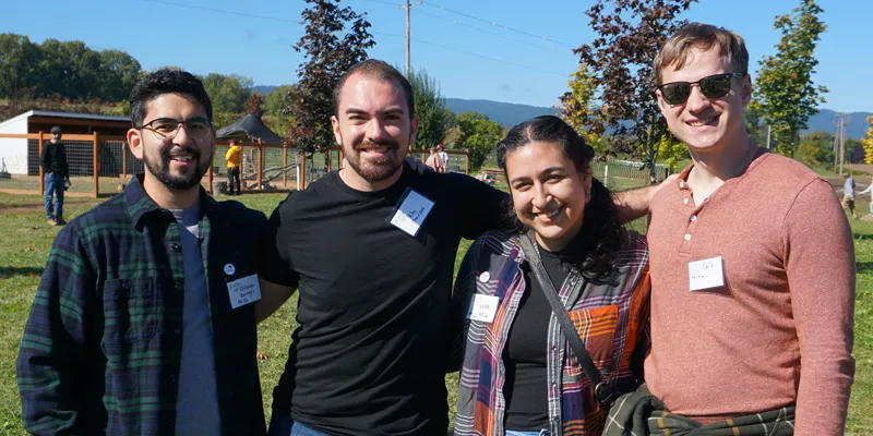 Four people standing with arms around each other, smiling.