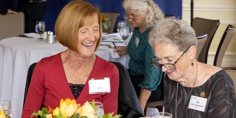 Two School of Nursing alumni seated together, laughing.