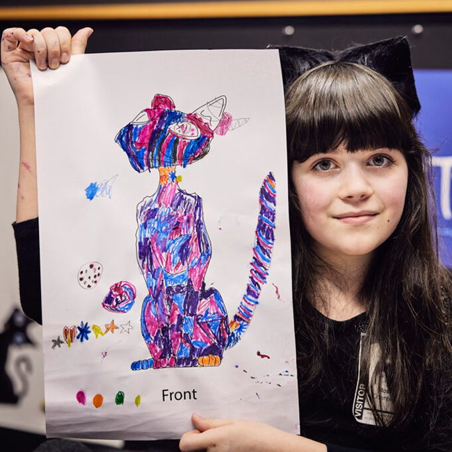 Rosie holds up a drawing of her cat statue