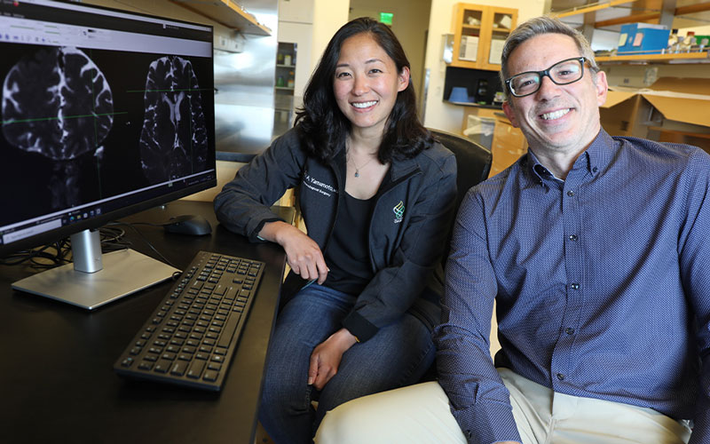 Erin Yamamoto, M.D., and Juan Piantino, M.D., sit in front of a computer monitor displaying brain images
