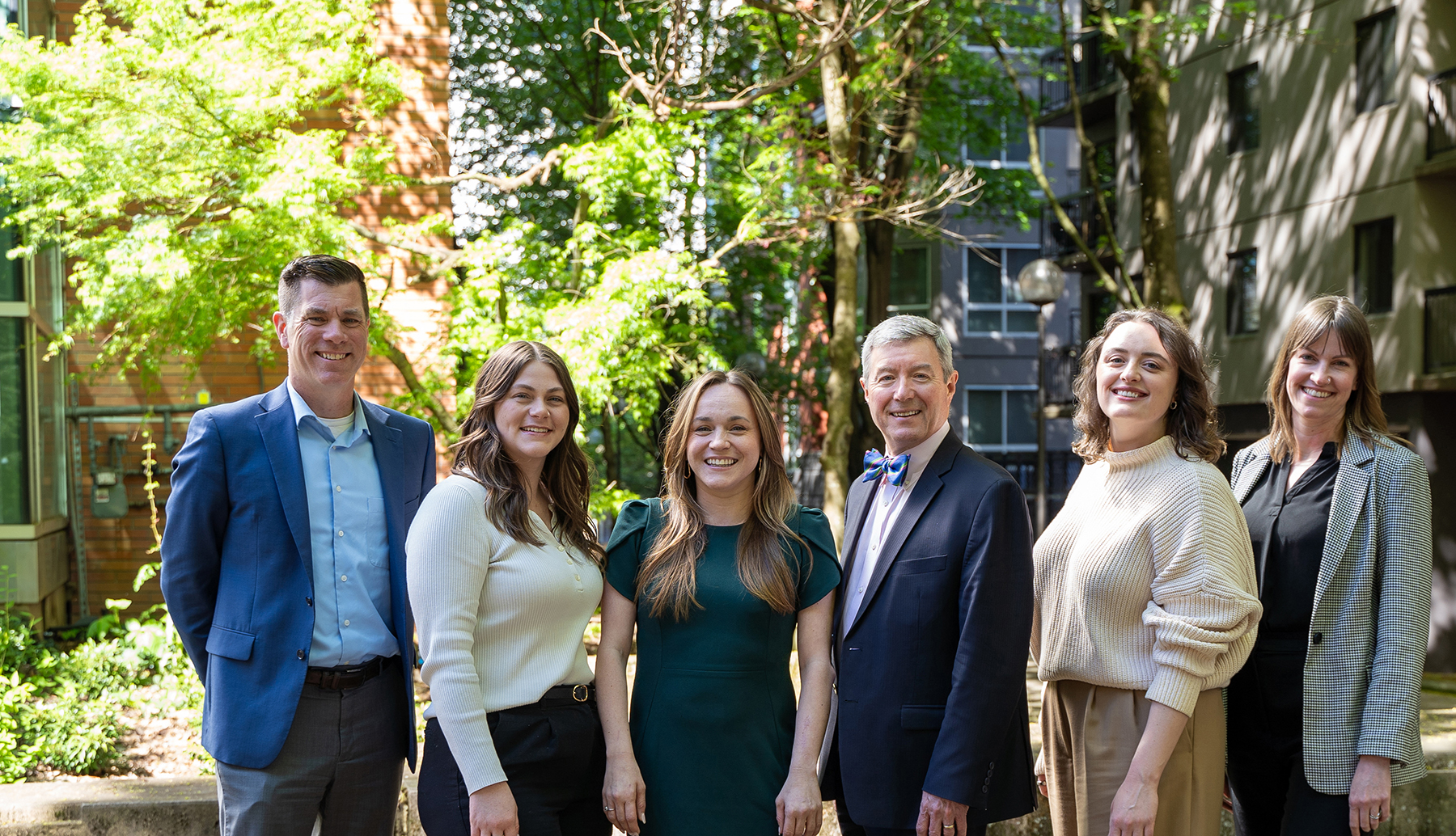 The OHSU Alumni Team standing together in a tree-lined courtyard wearing business attire.