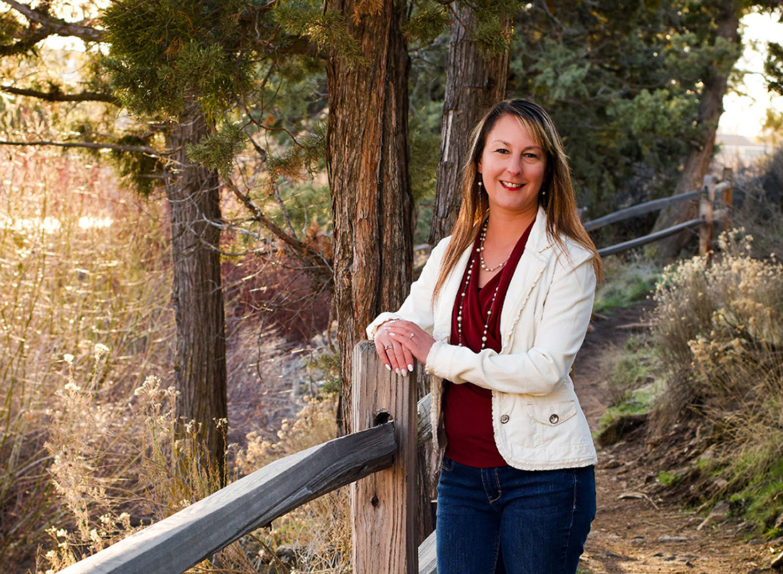 Amber La posing on a trail surrounded by trees.