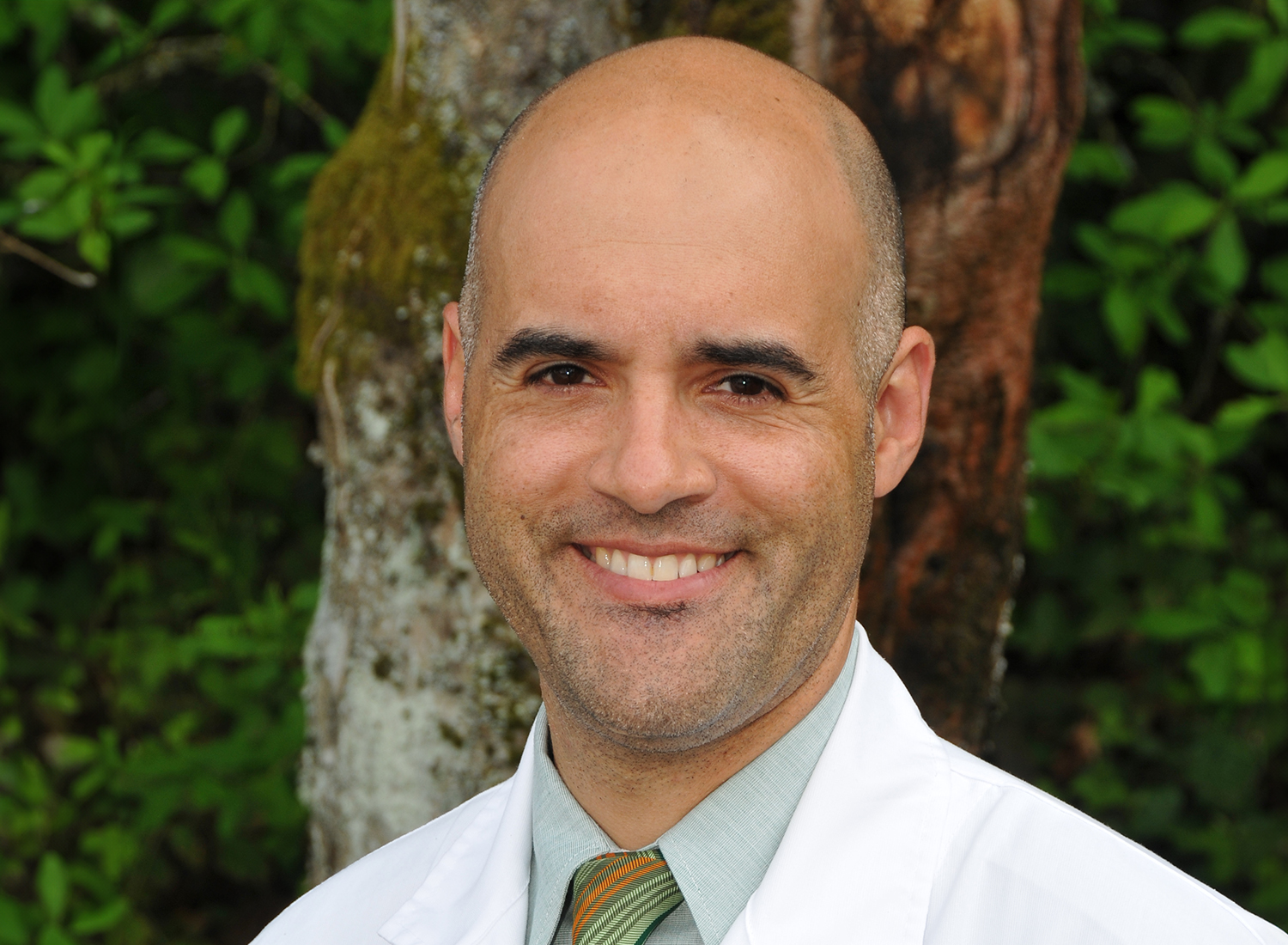 Clifford Coleman wearing a white coat and standing under a tree.