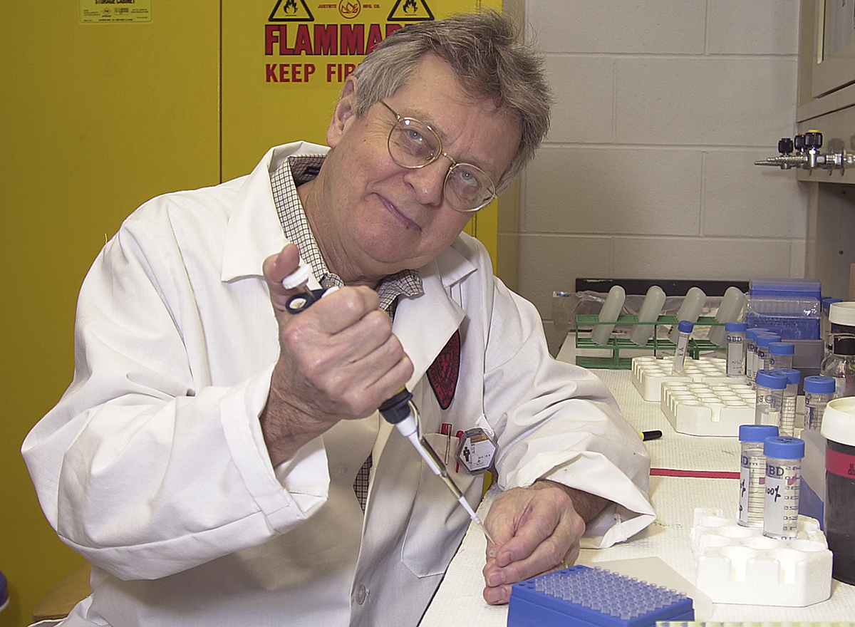 Daniel Nebert wearing a white coat sitting in a lab with test tubes