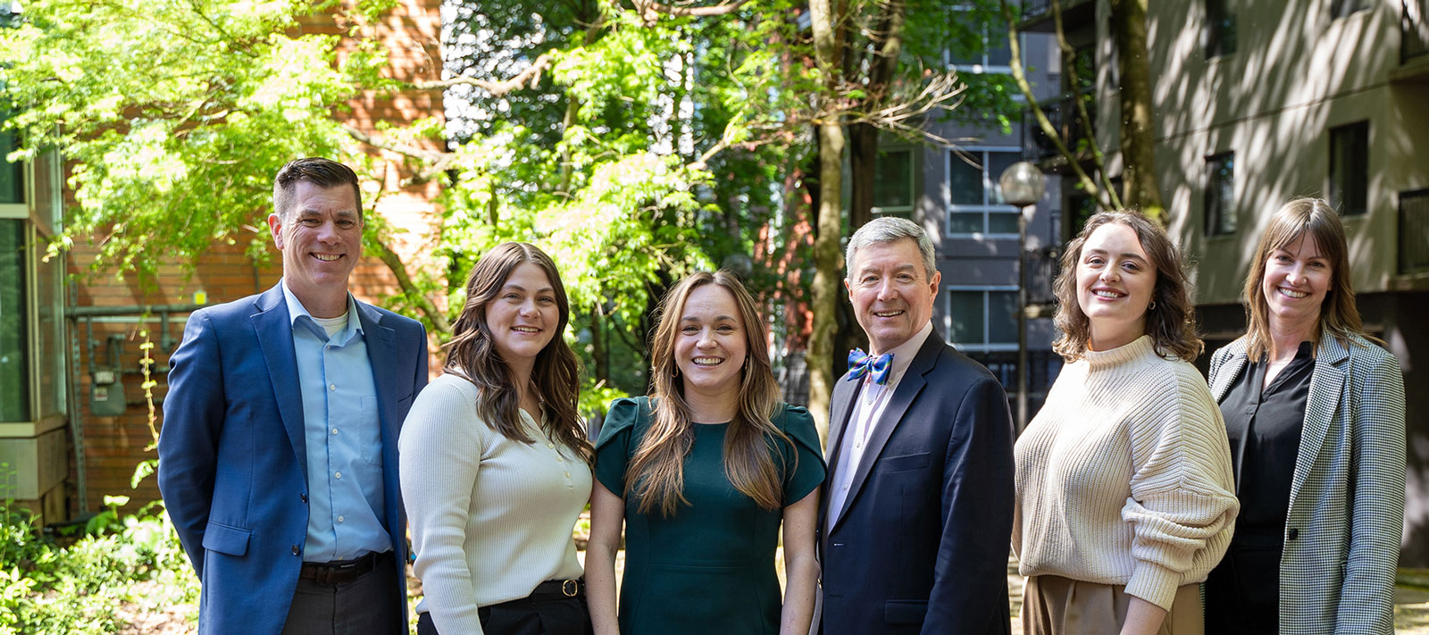 The OHSU Alumni Team standing together in a tree-lined courtyard wearing business attire.