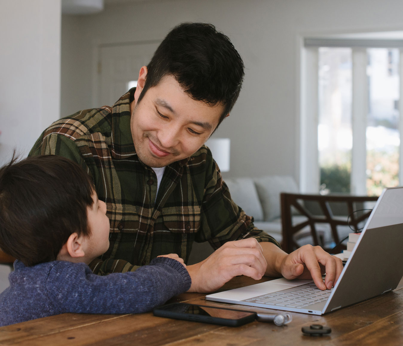 Man working at his laptop in the home smiles at his young child
