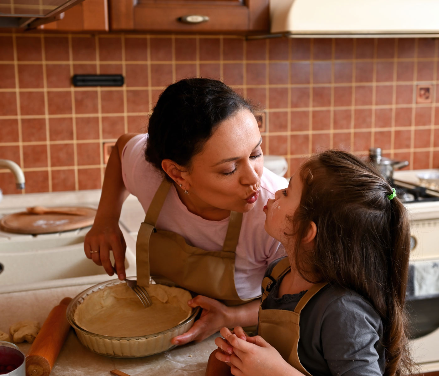 Woman kisses her dsaughter in the kitchen as they make a pie crust