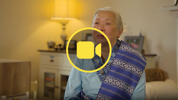 A woman wearing traditional Laotian formalwear speaks to a camera for an interview 