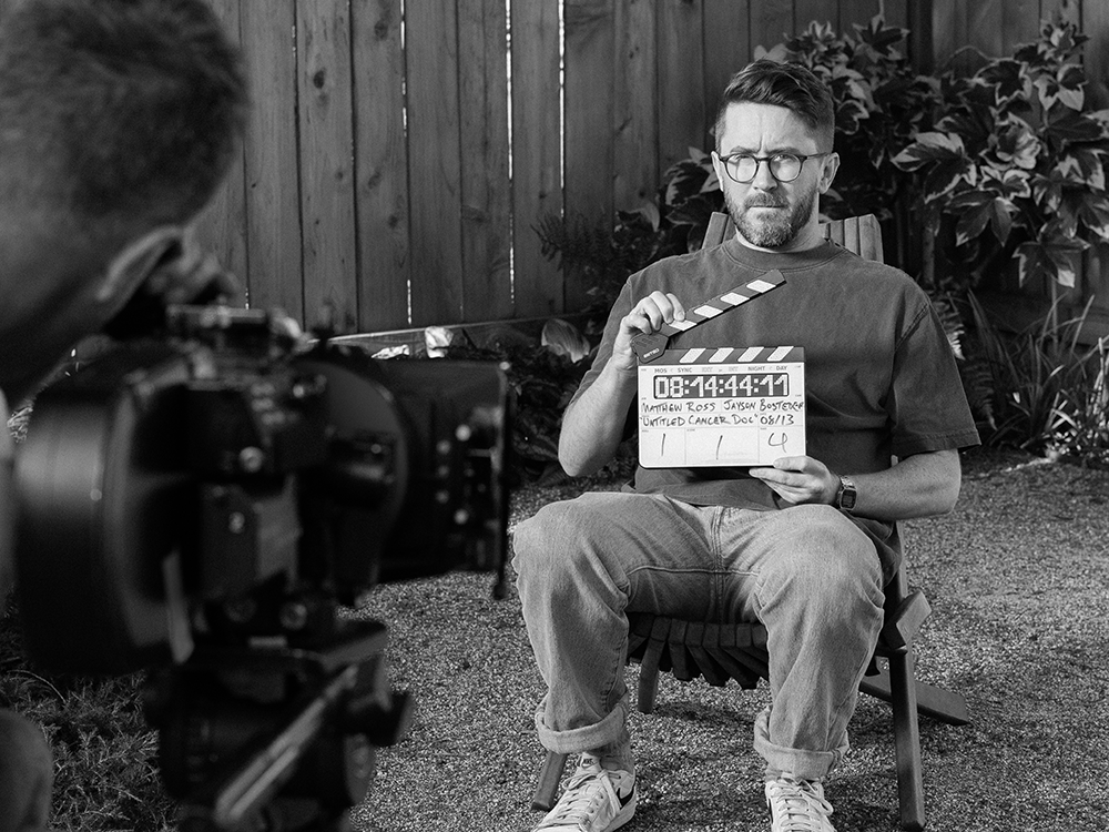 Matthew Ross sits in a chair holding a film slate.