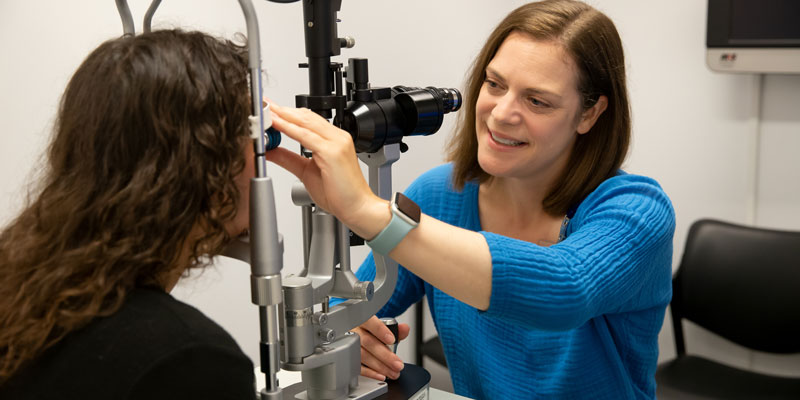 A doctor in a blue sweater examines a patient's eyes