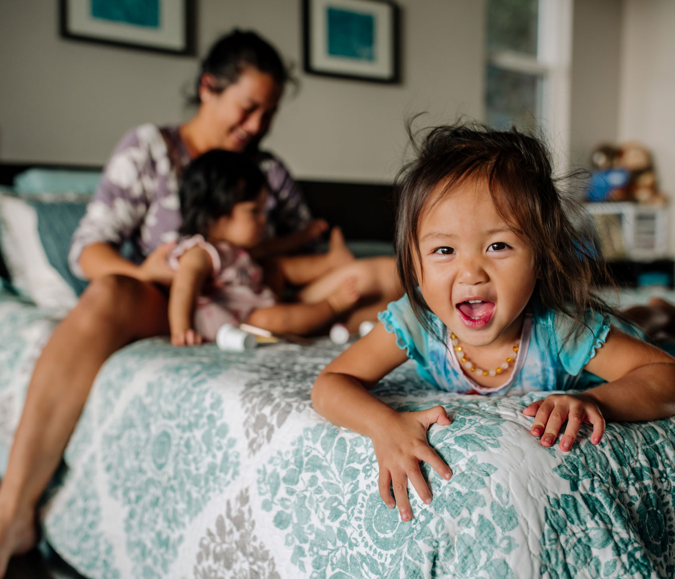 toddler playing on bed with mom and sibling