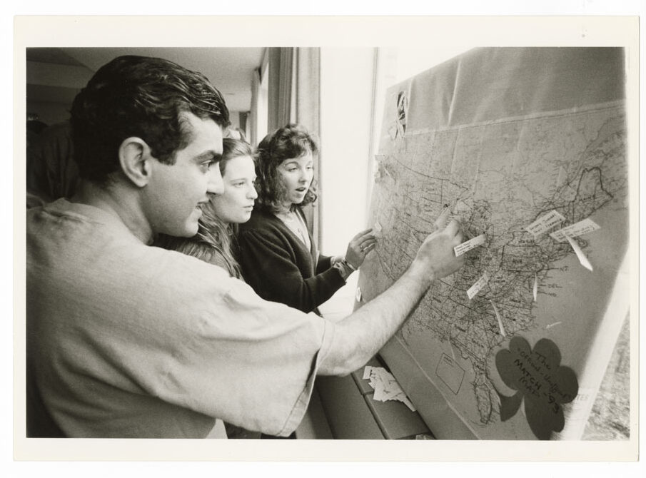 A black and white photo of a young man and two young women adding pins to a map on the wall.