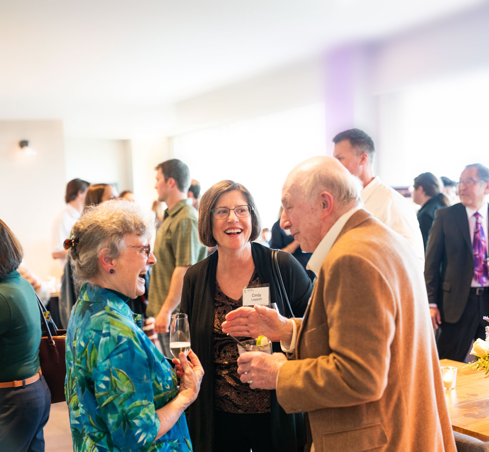 Two women and a man laughing together at a cocktail party.