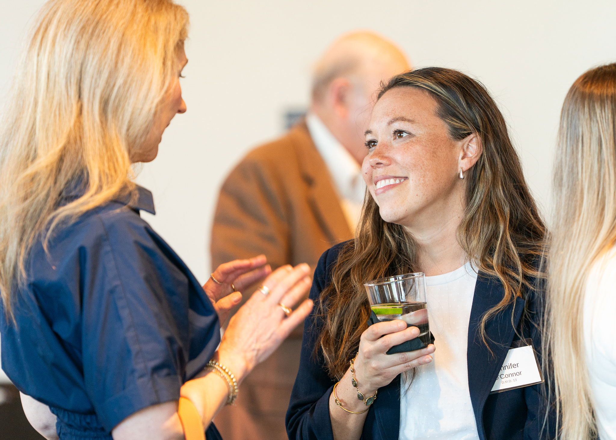 Two women in professional attire talking in a crowd of people.