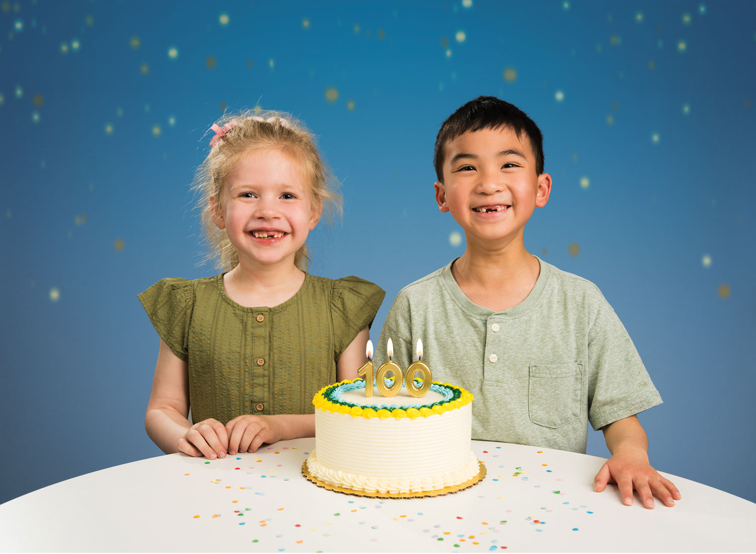 Two children with their baby teeth missing smile with a cake that has "100" candles.