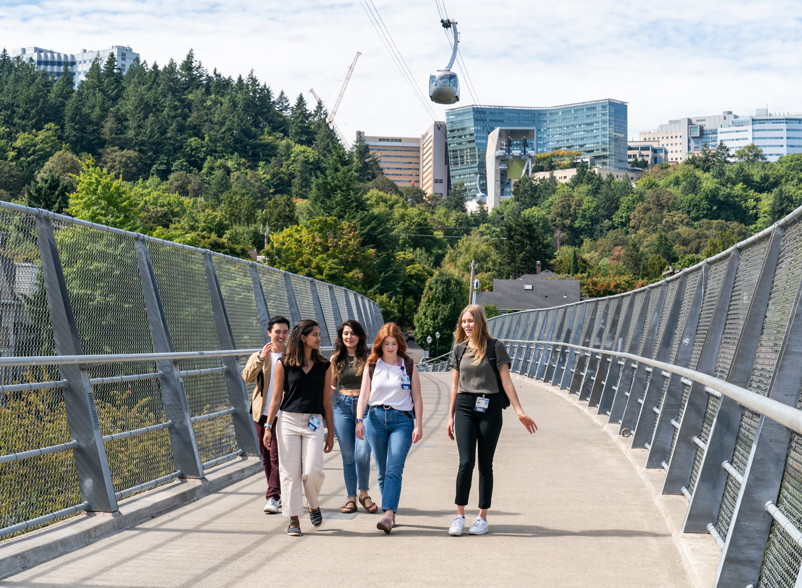 Four OHSU students walk across a bridge with the Portland aerial tram in the background.