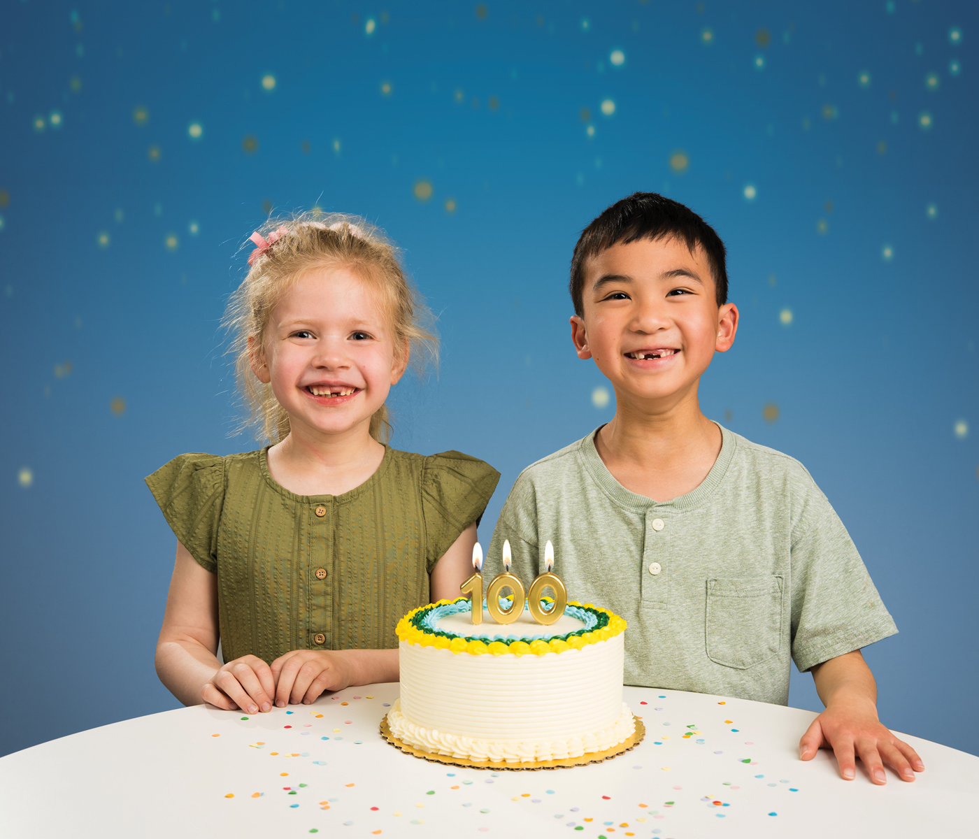 Two children with their baby teeth missing smile with a cake that has "100" candles.
